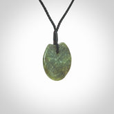 This piece is a small sized, oval round, disc pendant. It is suspended on a black coloured braided cord that is length adjustable.